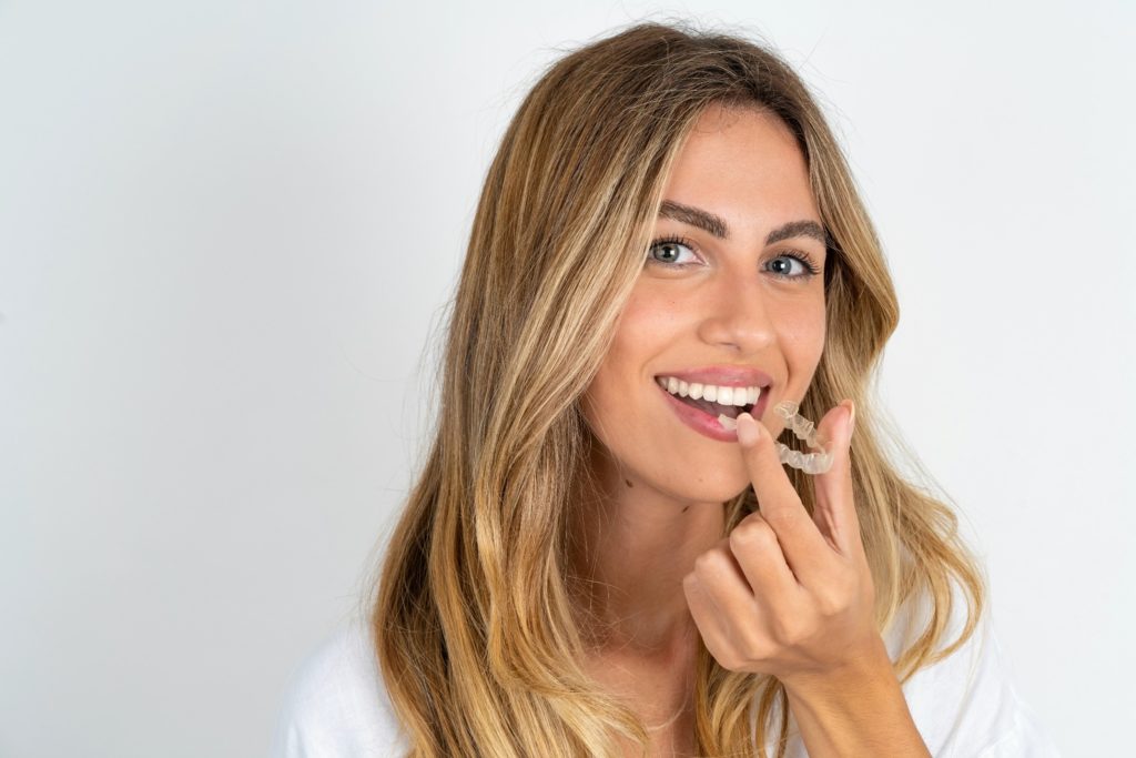 Woman smiling while placing clear aligners on her top teeth